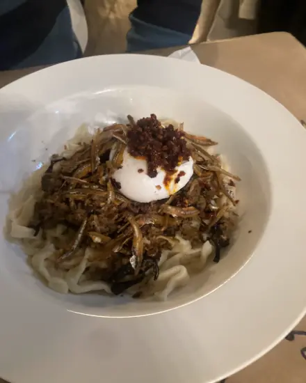Pan mee with a poached egg, crispy anchovies and minced pork in a white bowl