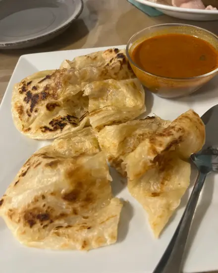 Golden flaky roti torn into pieces on a white plate with a glass bowl of curry