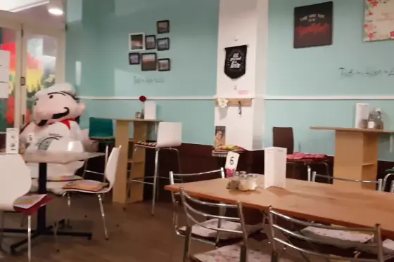 Long timber tables, framed pictures on the seafoam wall and a smiling chef figure by the door