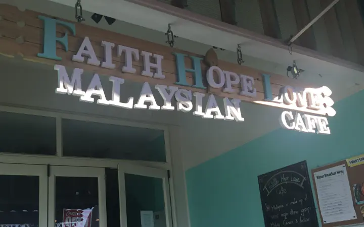 The Faith Hope Love sign at night: seafoam letters on a timber plank above the shopfront